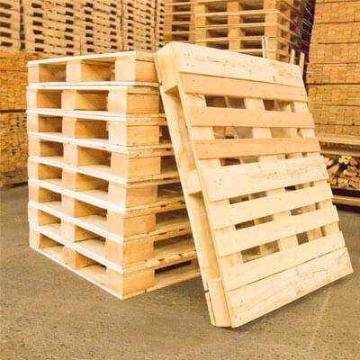 A stack of wooden 9 block grade pallets with one leaning against the stack.
